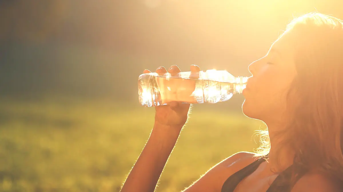 Woman drinking from a water bottle at sunset. About 20 years old Caucasian blonde in sports clothing.