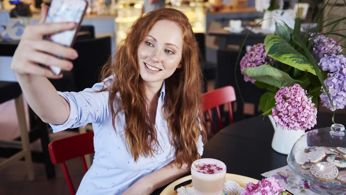 Smiling young woman taking a selfie in a cafe model released Symbolfoto property released PUBLICATIONxINxGERxSUIxAUTxHUNxONLY ABIF00878  
