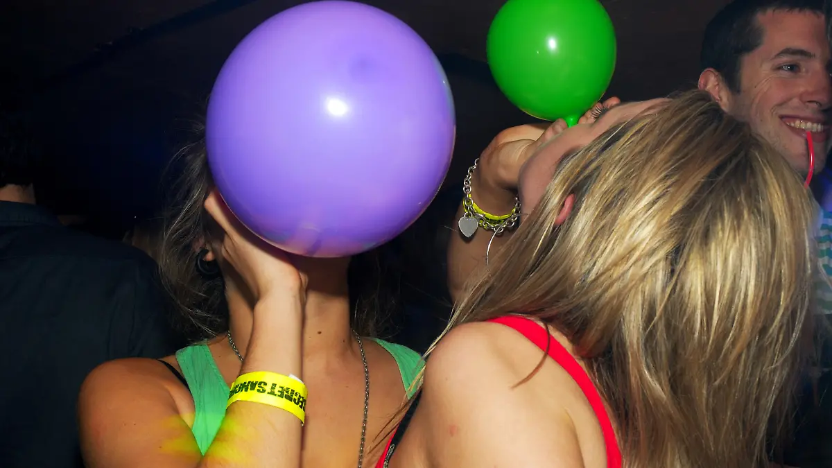 Zwei Frauen ihnalieren Lachgas aus bunten Luftballons.
