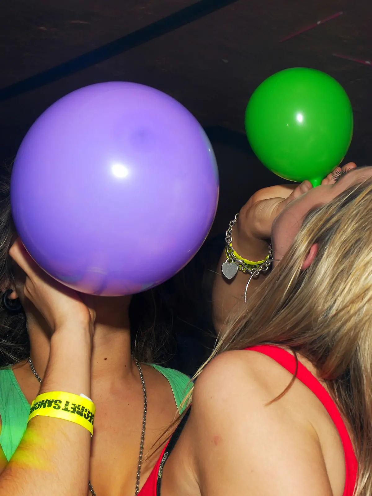 Zwei Frauen ihnalieren Lachgas aus bunten Luftballons.
