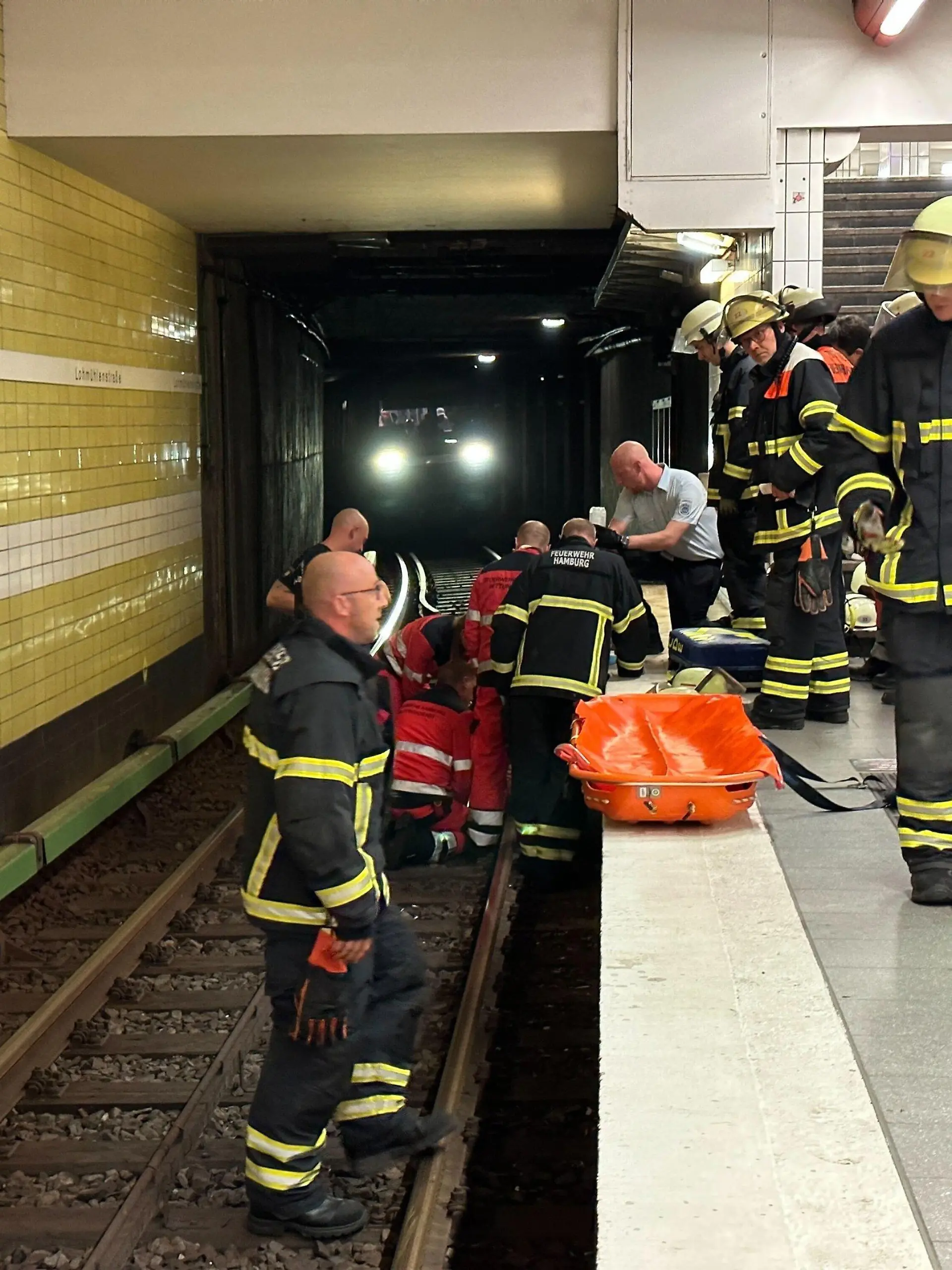 15.08.2023, Hamburg: Feuerwehrleute bei der Rettungsarbeiten am U-Bahnhof Lohmühlenstraße. Dank des schnellen Reagierens der Mitarbeiter der U-Bahnwache in Hamburg konnte einem älteren Herren am Dienstagabend das Leben gerettet werden. Nach seinem Sturz ins Gleisbett schoben ihn die Helfer in einen Hohlrraum unter dem Bahnsteig und stoppten den Zug. Foto: Steven Hutchigs/dpa +++ dpa-Bildfunk +++