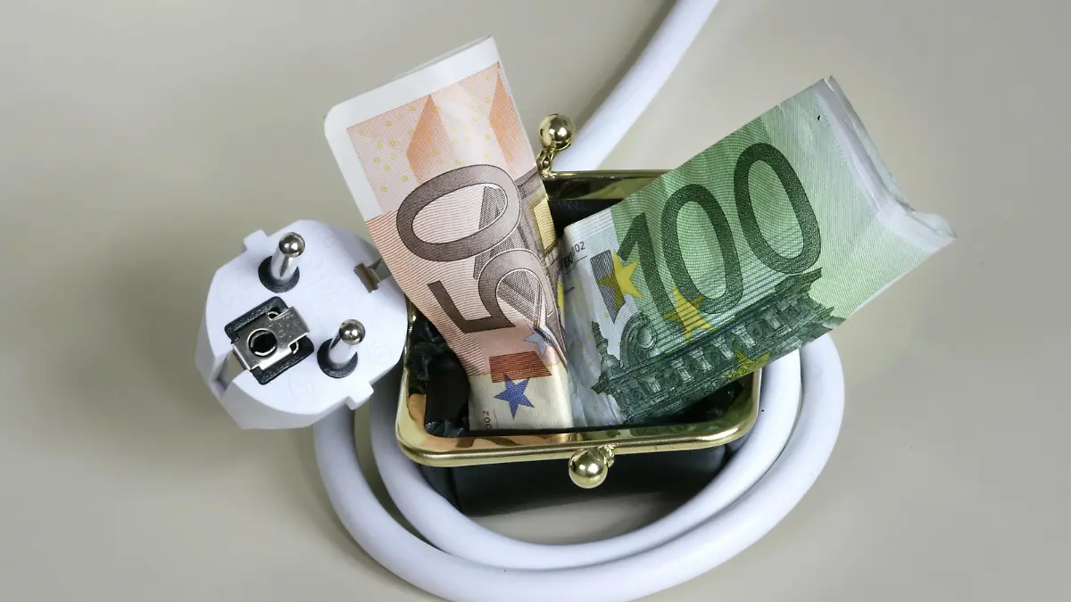 Stromkabel ist um ein Portemonnaie geschlungen, aus dem Geldscheine hervorquellen. Symbol: hohe Energiepreise stellen eine finanzielle Belastung für die Verbraucher dar. Power plug wrapped around a purse. Power plug wrapped around a purse  