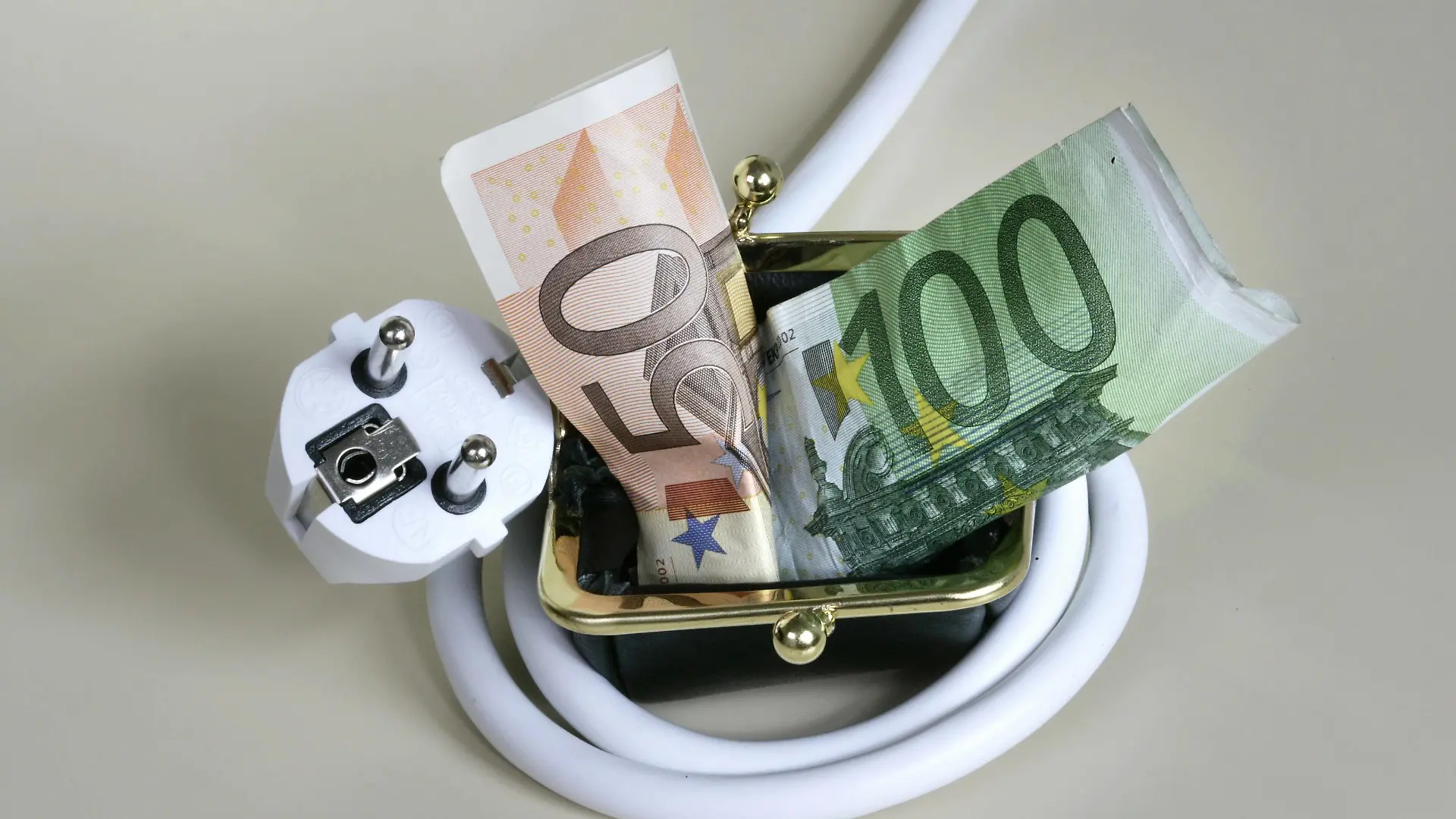 Stromkabel ist um ein Portemonnaie geschlungen, aus dem Geldscheine hervorquellen. Symbol: hohe Energiepreise stellen eine finanzielle Belastung für die Verbraucher dar. Power plug wrapped around a purse. Power plug wrapped around a purse