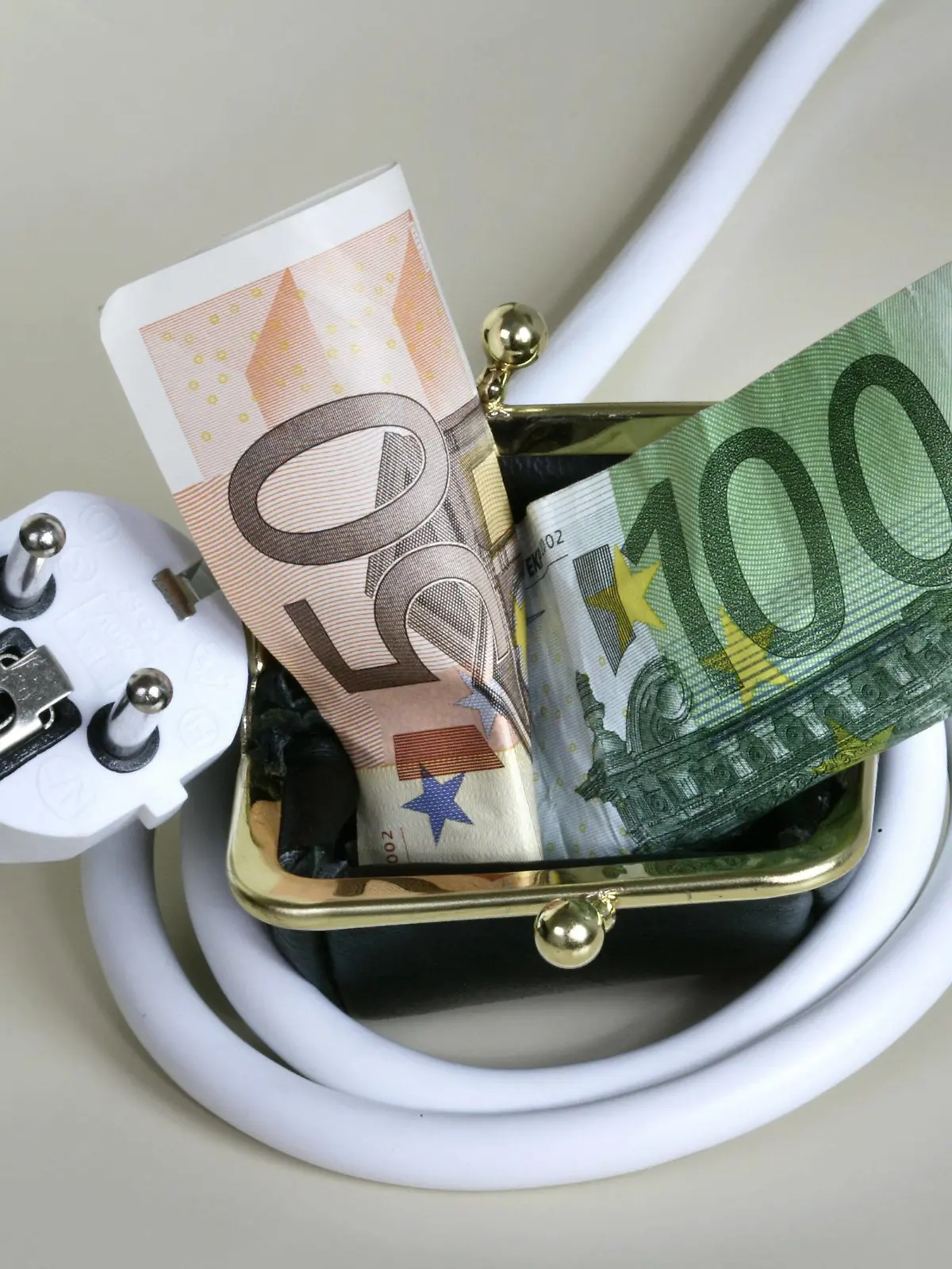 Stromkabel ist um ein Portemonnaie geschlungen, aus dem Geldscheine hervorquellen. Symbol: hohe Energiepreise stellen eine finanzielle Belastung für die Verbraucher dar. Power plug wrapped around a purse. Power plug wrapped around a purse  