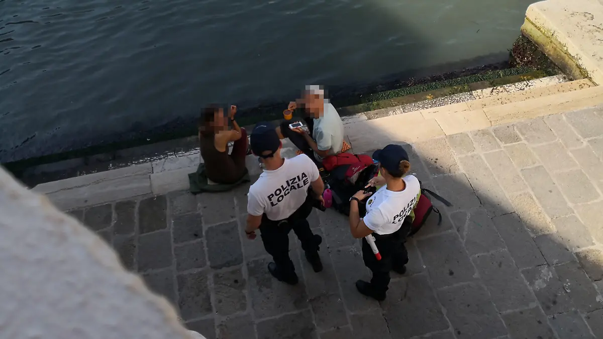 HANDOUT - 19.07.2019, Italien, Venedig: Zwei deutsche Touristen werden von zwei Polizisten an der Treppe der Rialto-Brücke angesprochen, da sie sich mit einem kleinen Kaffeekocher Kaffee auf dem Gehweg zubereitet haben. (zu dpa «Deutsche Touristen kochen Kaffee in Venedig - fast 1000 Euro Strafe») Foto: Comune di Venezia/dpa - ACHTUNG: Nur zur redaktionellen Verwendung im Zusammenhang mit der aktuellen Berichterstattung und nur mit vollständiger Nennung des vorstehenden Credits +++ dpa-Bildfunk +++