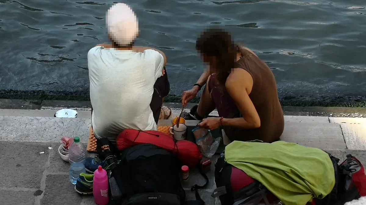HANDOUT - 19.07.2019, Italien, Venedig: Zwei deutsche Touristen sitzen mit ihrem Gepäck an der Treppe der Rialto-Brücke und kochen sich mit einem kleinen Kaffeekocher einen Kaffee auf dem Gehweg. (zu dpa "Deutsche Touristen kochen Kaffee in Venedig - fast 1000 Euro Strafe") Foto: Comune di Venezia/dpa - ACHTUNG: Nur zur redaktionellen Verwendung im Zusammenhang mit der aktuellen Berichterstattung und nur mit vollständiger Nennung des vorstehenden Credits +++ dpa-Bildfunk +++