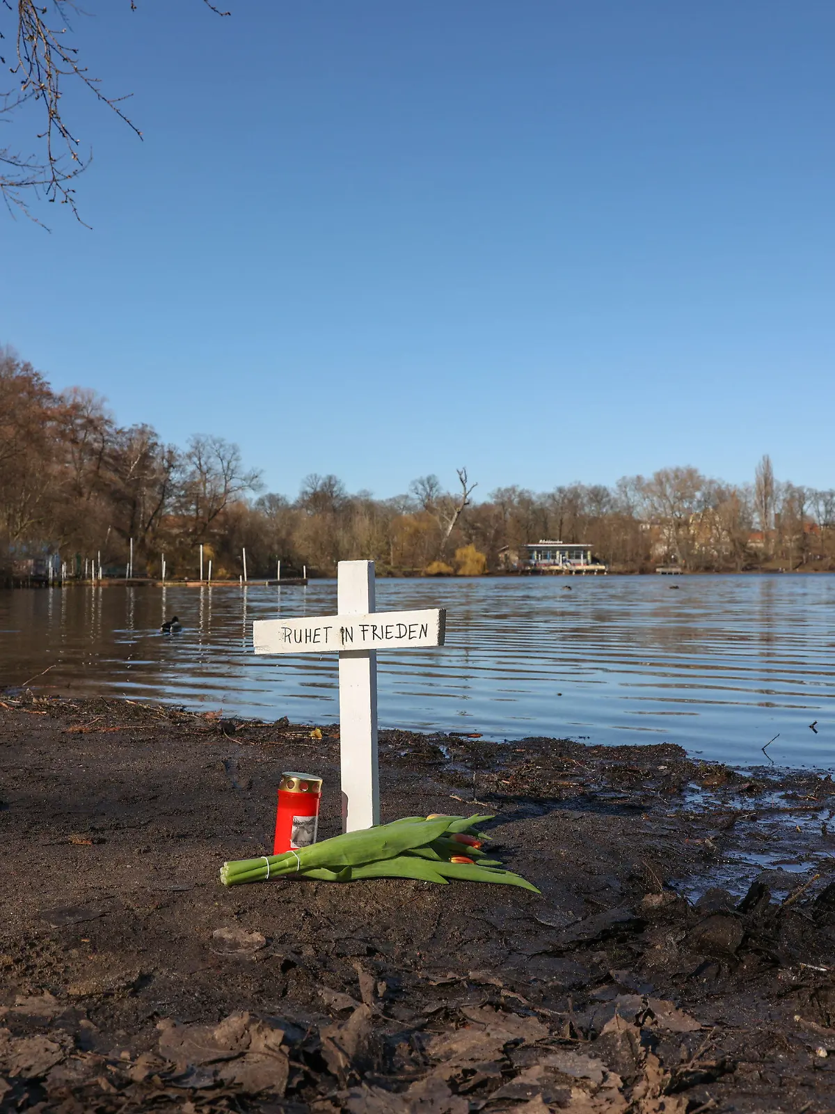28.02.2023, Berlin: Nach dem Fund zweier Leichen im Weißen See sind an dem Fundort ein Kreuz, Blumen und eine Kerze zu sehen. Foto: Jörg Carstensen/dpa +++ dpa-Bildfunk +++