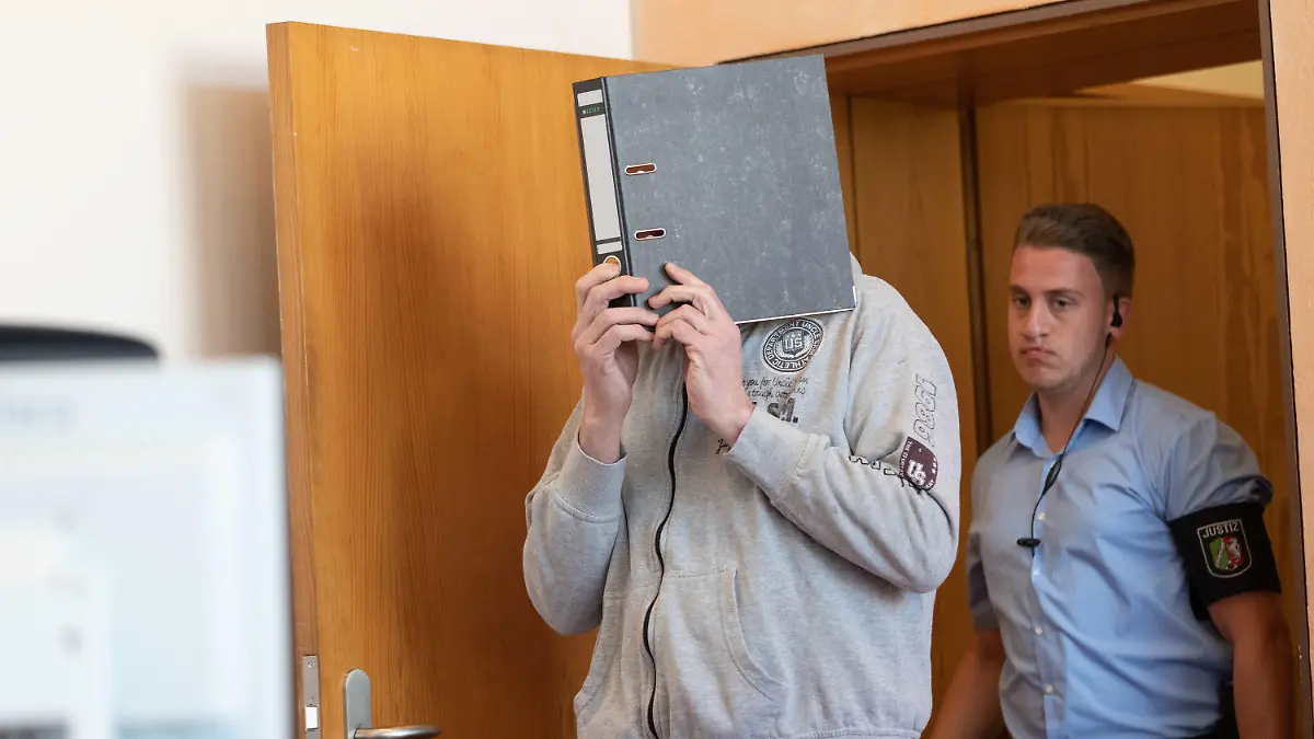 05.07.2019, Nordrhein-Westfalen, Detmold: Einer der Angeklagten kommt mit einem Aktenordner vor dem Gesicht und in Begleitung eines Justizbeamten in einen Saal des Landgerichtes. Der Prozess um den hundertfachen sexuellen Missbrauch auf einem Campingplatz bei Lügde wird mit einem Verhandlungstag fortgesetzt. Weitere Opfer und Angehörige sagen als Zeugen aus. Foto: Friso Gentsch/dpa +++ dpa-Bildfunk +++