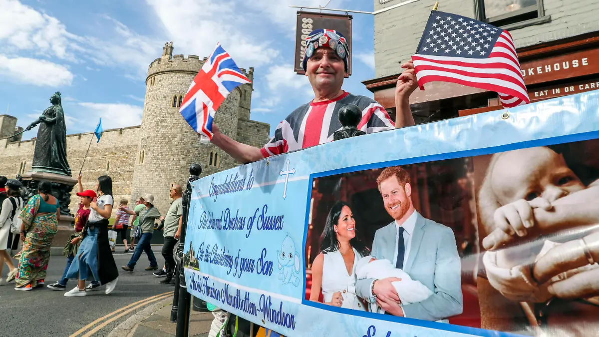 05.07.2019, Großbritannien, Windsor: John Loughrey, Fan der britischen Königsfamilie, steht hinter einem Banner, das ein Bild von Prinz Harry und Herzogin Meghan mit ihrem Sohn Archie zeigt. Archie wird am Samstag, den 05.07.2019, in Windsor getauft. Die Zeremonie soll in einem kleinen Kreis stattfinden. Foto: Steve Parsons/PA Wire/dpa +++ dpa-Bildfunk +++