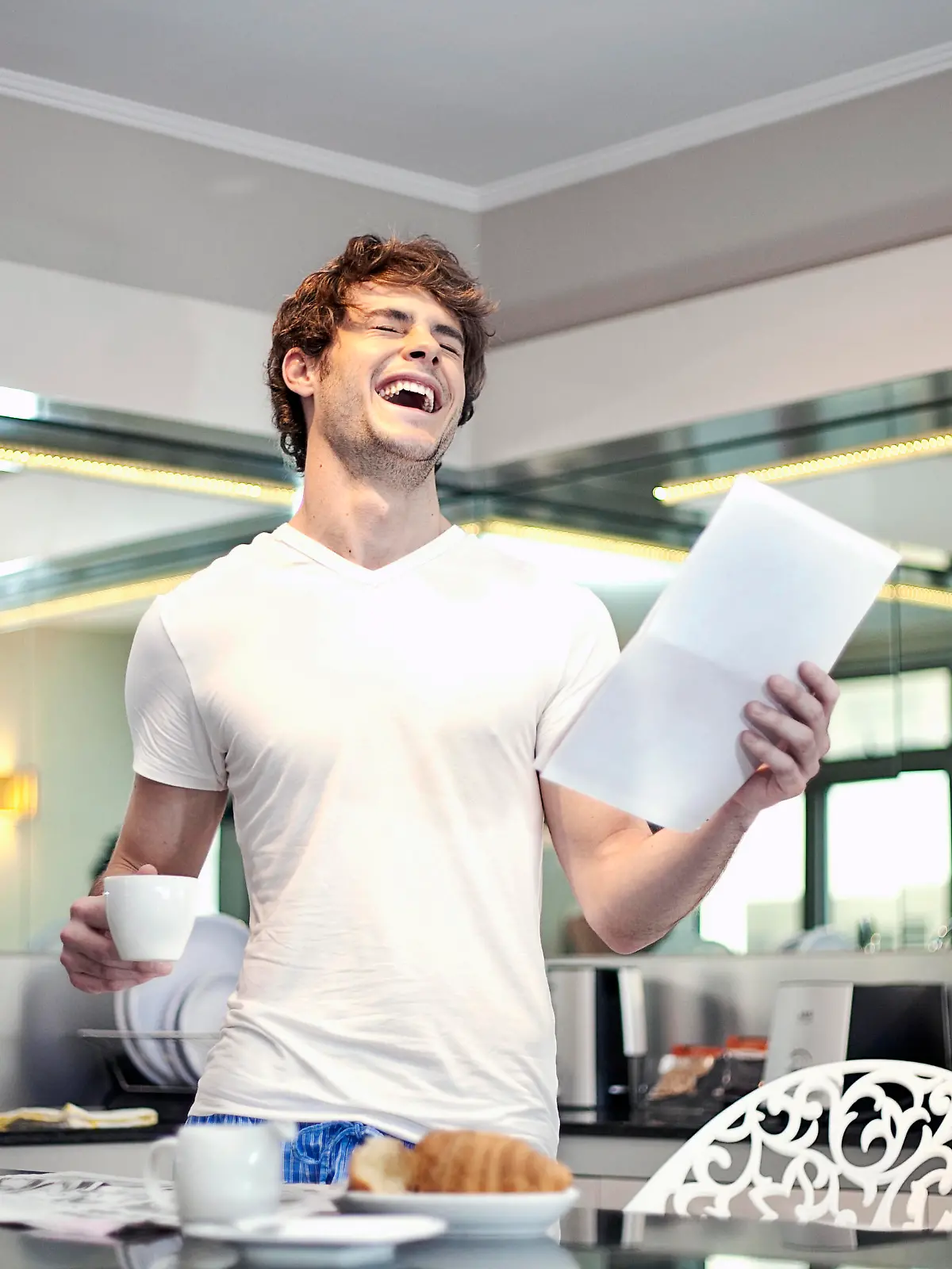 Happy man with letter laughing while holding coffee cup at kitchen || Modellfreigabe vorhanden