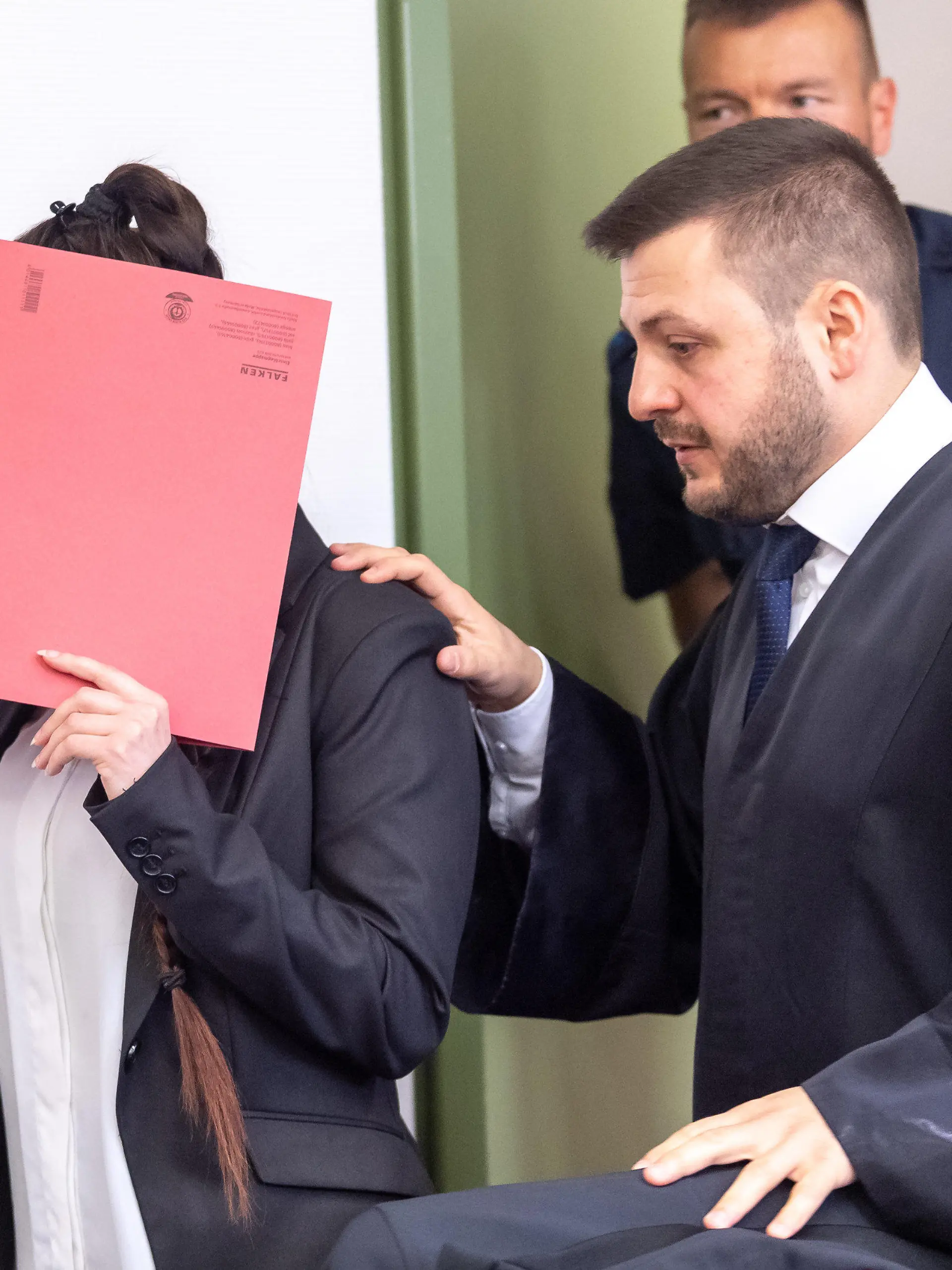 ARCHIV - 09.04.2019, Bayern, München: Die Angeklagte hält sich beim Betreten des Gerichtssaals einen roten Aktendeckel vor ihr Gesicht. Rechts steht ihr Anwalt Ali Aydin. Der Frau wird unter anderem vorgeworfen, ein fünf Jahre altes Mädchen als Sklavin gehalten und verdursten lassen zu haben. Foto: Peter Kneffel/dpa +++ dpa-Bildfunk +++