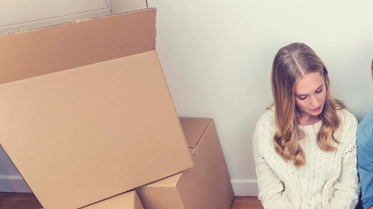 Young couple sitting in new house with packing boxes. They look like they have just moved in and they are very happy, smiling and talking. They are using a digital tablet, sitting on the floor in casual clothes. Copy space.