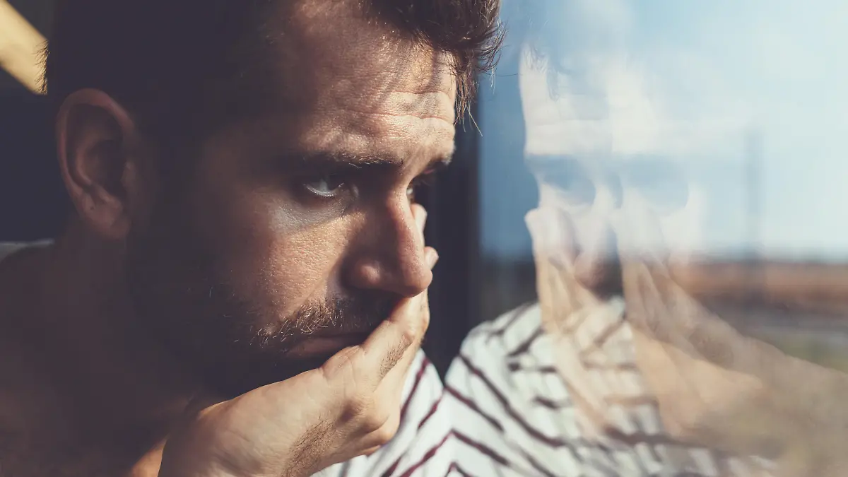 Sad young man looking through the window