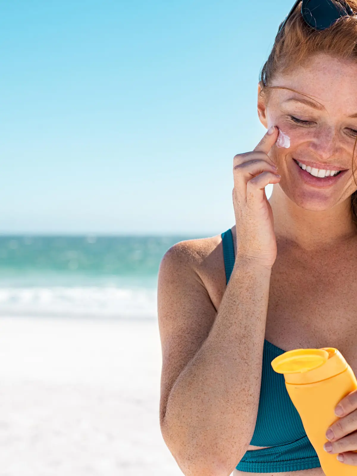 Rothaarige Frau cremt sich mit Sonnencreme ein