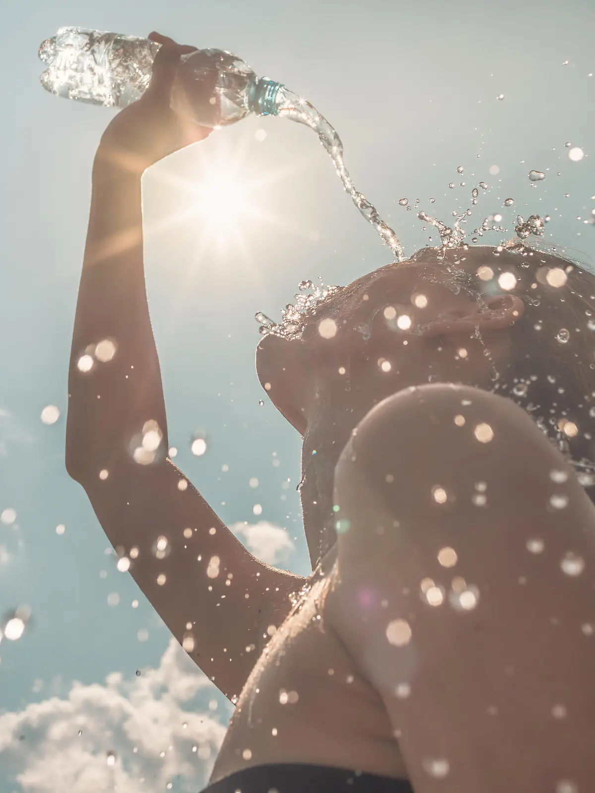 Woman cooling down splashing herself with bottle of water on a hot sunny day.