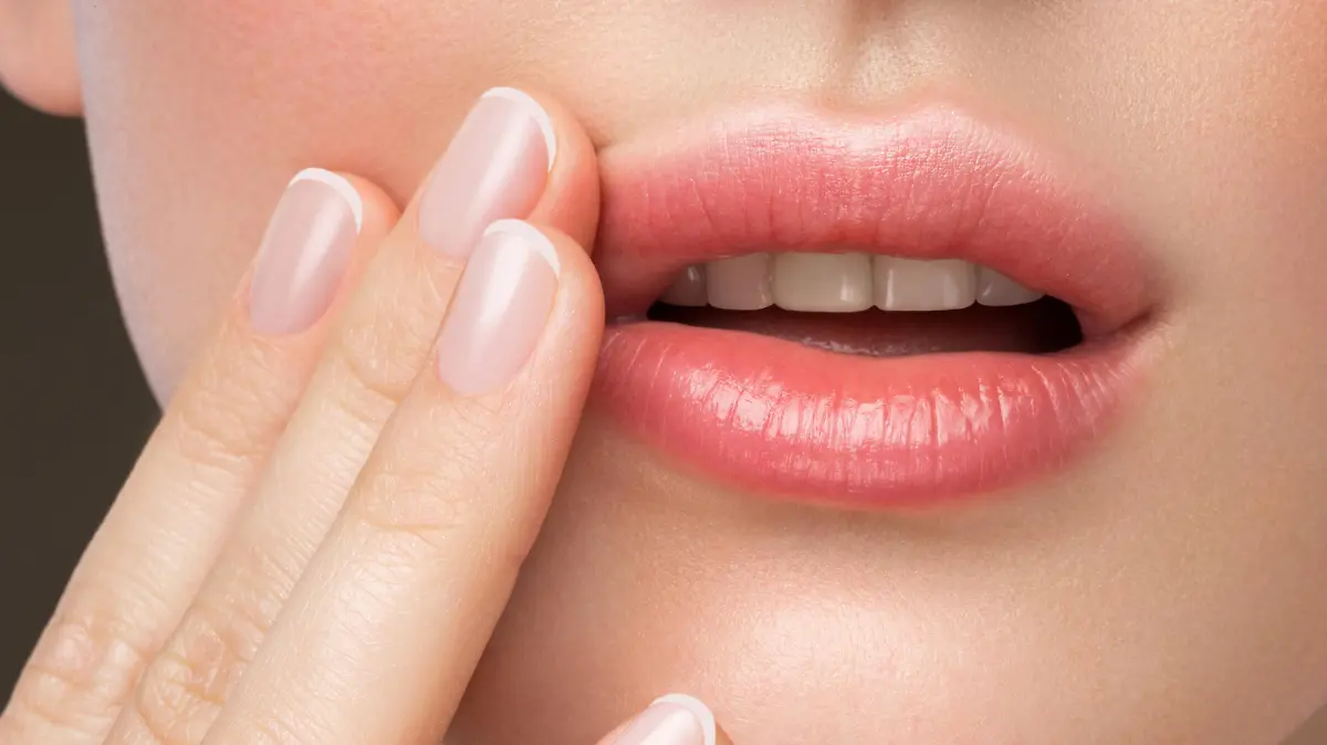 Frau fasst sich an Lippe mit Aphthe.