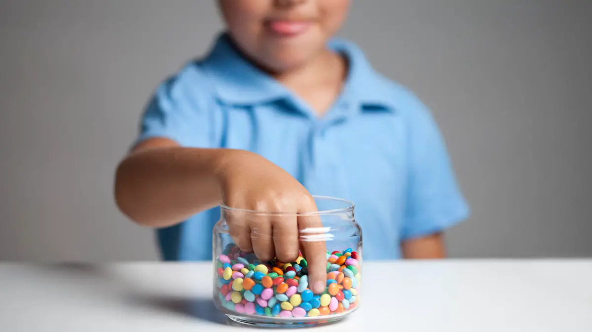 Little boy licking his lips while taking candy from the candy jar.