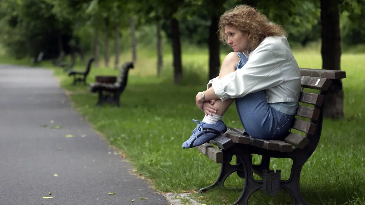 Berlin: Eine Frau sitzt allein mit angezogenen Beinen auf einer Parkbank in einer Grünanlage in Berlin, aufgenommen am 16.06.2004 (Illustration zum Thema Einsamkeit, Alleinsein, Körpersprache, Isolation, Depression). Körperhaltung und Mimik drücken grüblerische Nachdenklichkeit und persönliche Isolation aus.