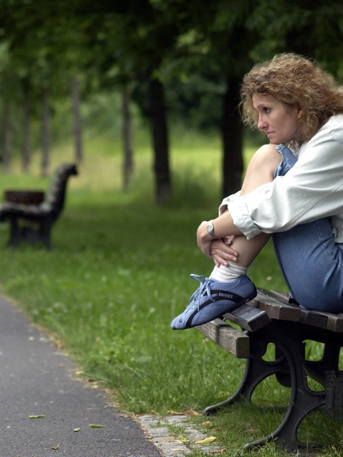 Berlin: Eine Frau sitzt allein mit angezogenen Beinen auf einer Parkbank in einer Grünanlage in Berlin, aufgenommen am 16.06.2004 (Illustration zum Thema Einsamkeit, Alleinsein, Körpersprache, Isolation, Depression). Körperhaltung und Mimik drücken grüblerische Nachdenklichkeit und persönliche Isolation aus.