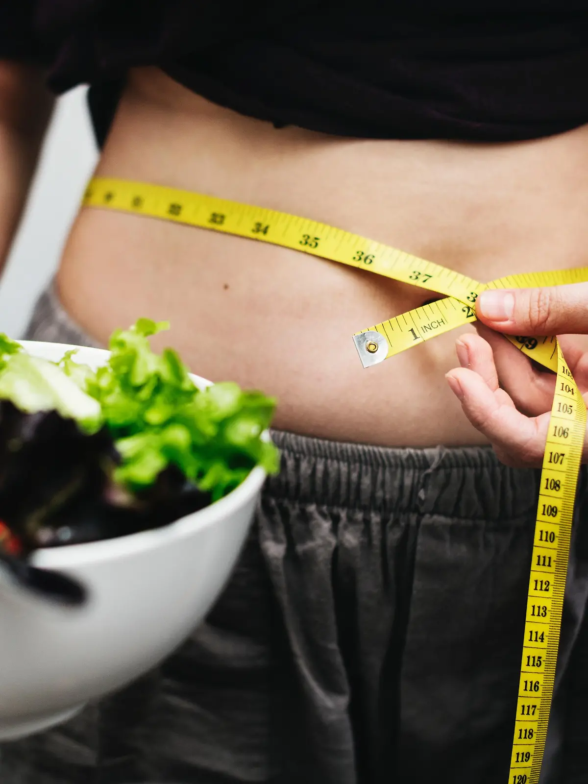 Frau mit Salat und Maßband um den Bauch