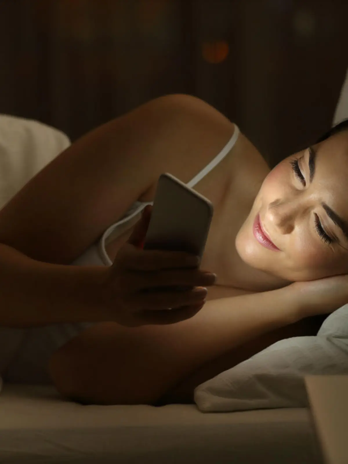 Junge Frau liegt mit Smartphone im Bett
