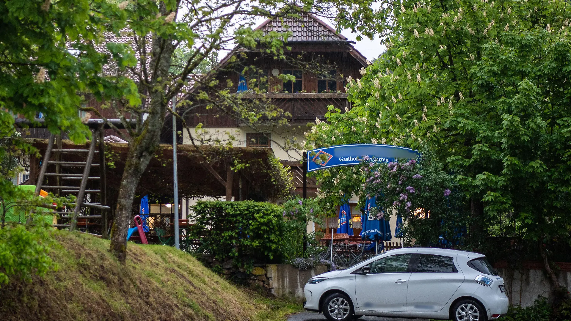 11.05.2019, Bayern, Passau: Eine Pension steht nahe der Ilz zwischen Bäumen. Drei tote Personen sind in einem Zimmer der Pension gefunden worden. Den Angaben zufolge stammen die Toten aus Niedersachsen und Rheinland-Pfalz. Es sei noch völlig offen, wie die drei Menschen ums Leben kamen, sagte ein Sprecher der Polizei. Foto: Lino Mirgeler/dpa - ACHTUNG: Das Schild an der Pension und Aufkleber am Auto wurden aus rechtlichen Gründen gepixelt +++ dpa-Bildfunk +++