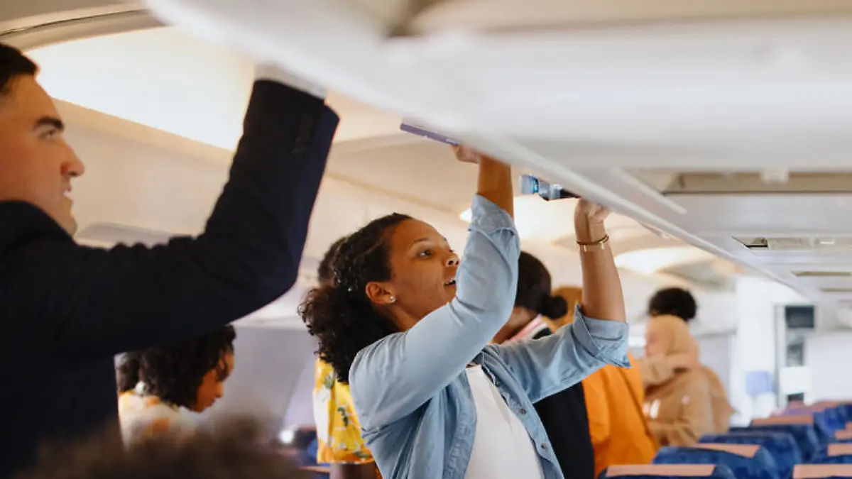 Cabin Crew helps passenger with putting bags and suitcases in overhead locker