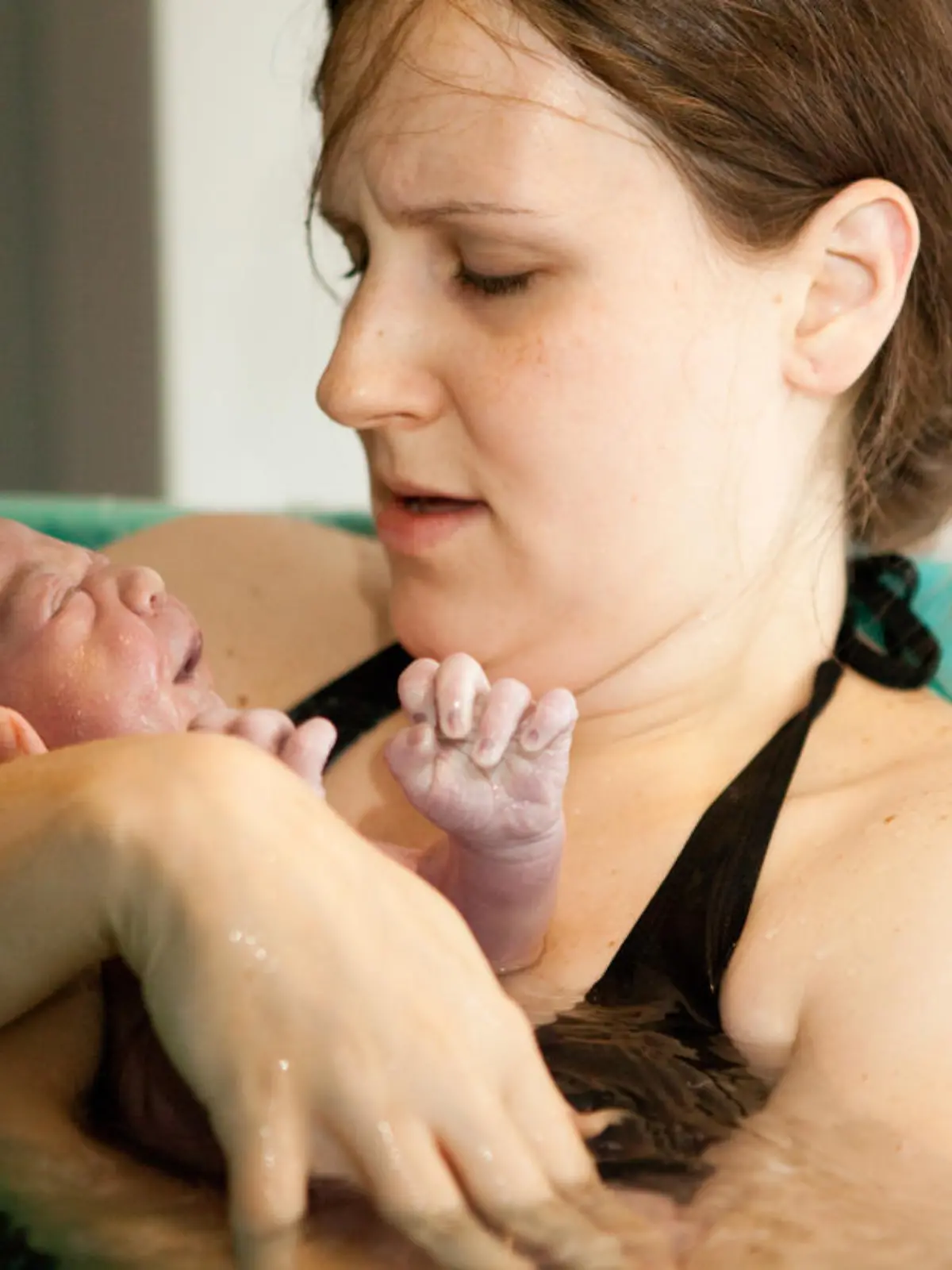 Mutter hält Baby in Wanne nach Hausgeburt