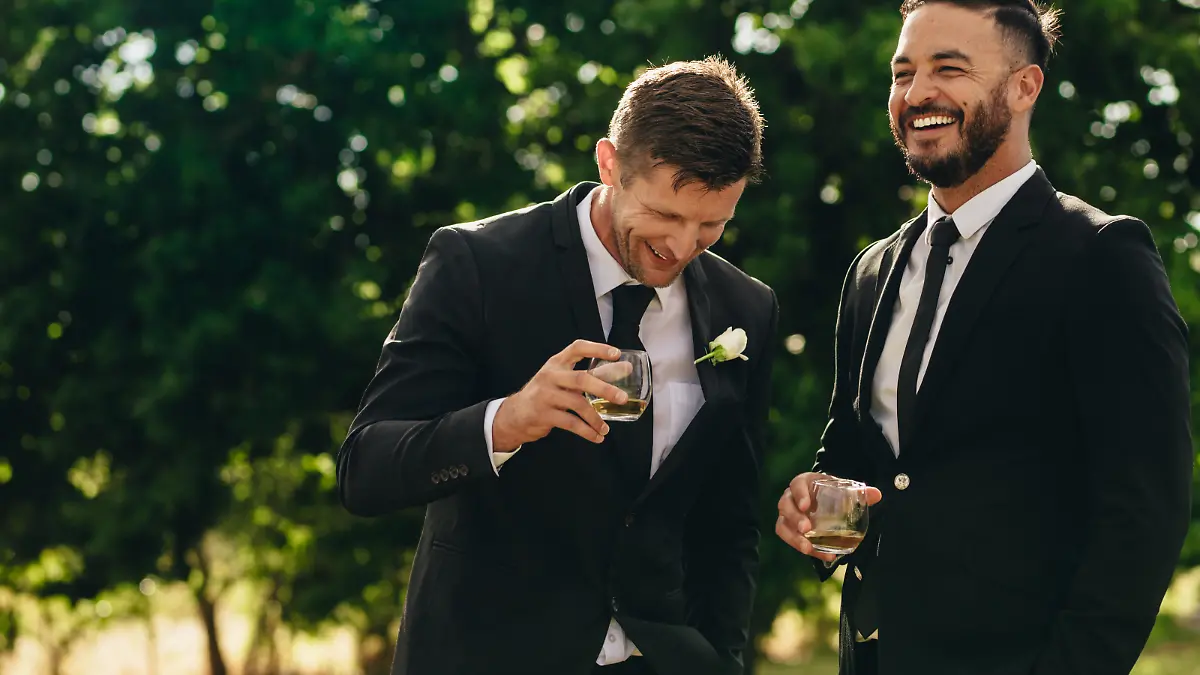 Groom and best man drinking and smiling during wedding party. Groom and groomsmen partying after wedding.