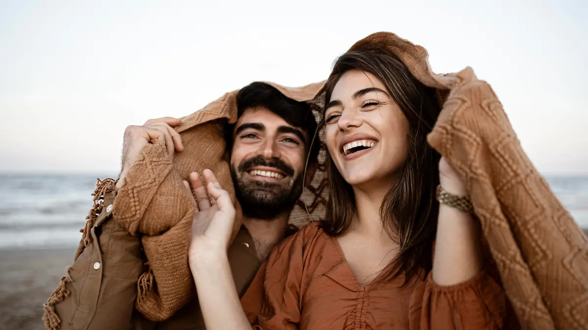Cheerful young couple covering blanket at beach model released Symbolfoto RCPF01236 