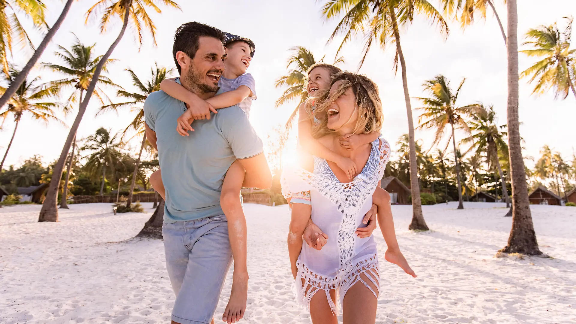 Happy parents and their small kids having fun while piggybacking on the beach in summer day.