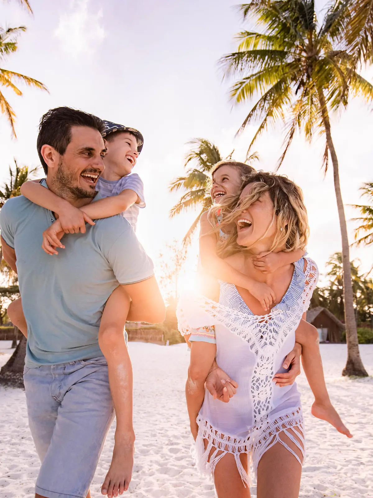 Happy parents and their small kids having fun while piggybacking on the beach in summer day.