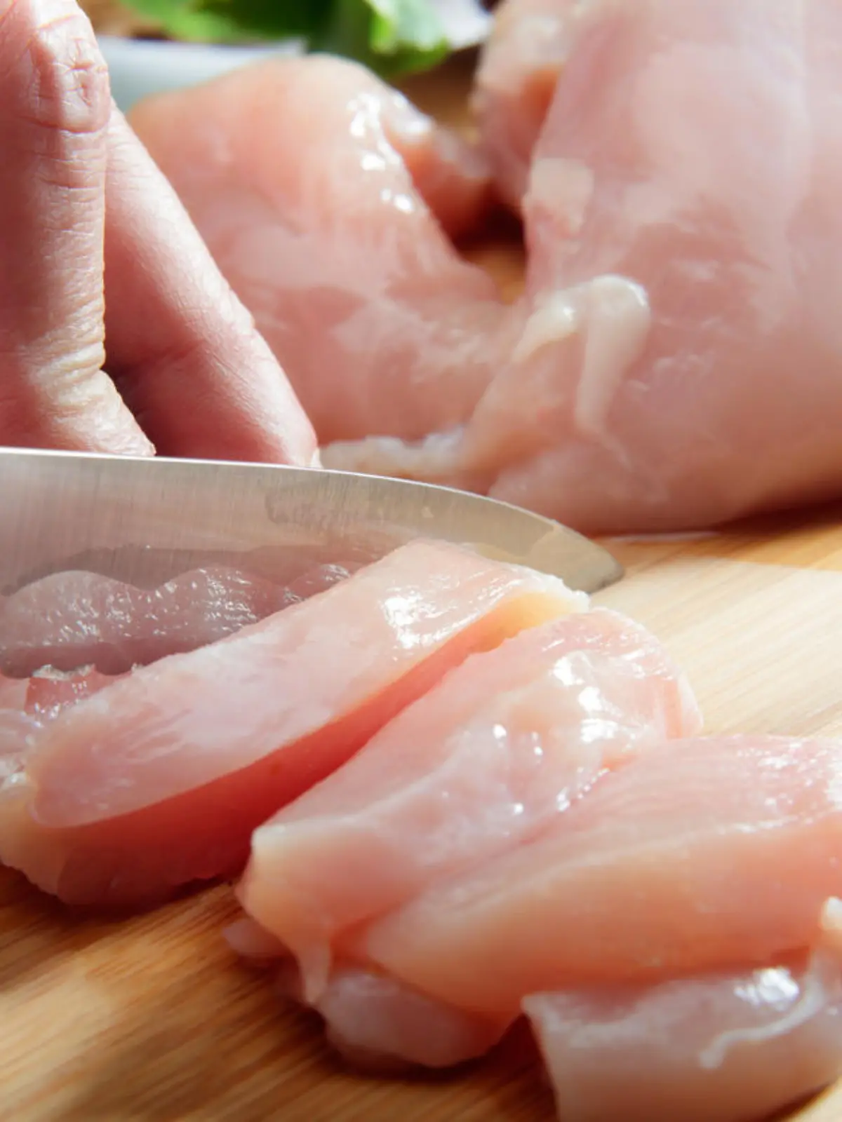 Man's hand cutting raw chicken breast. Selective focus