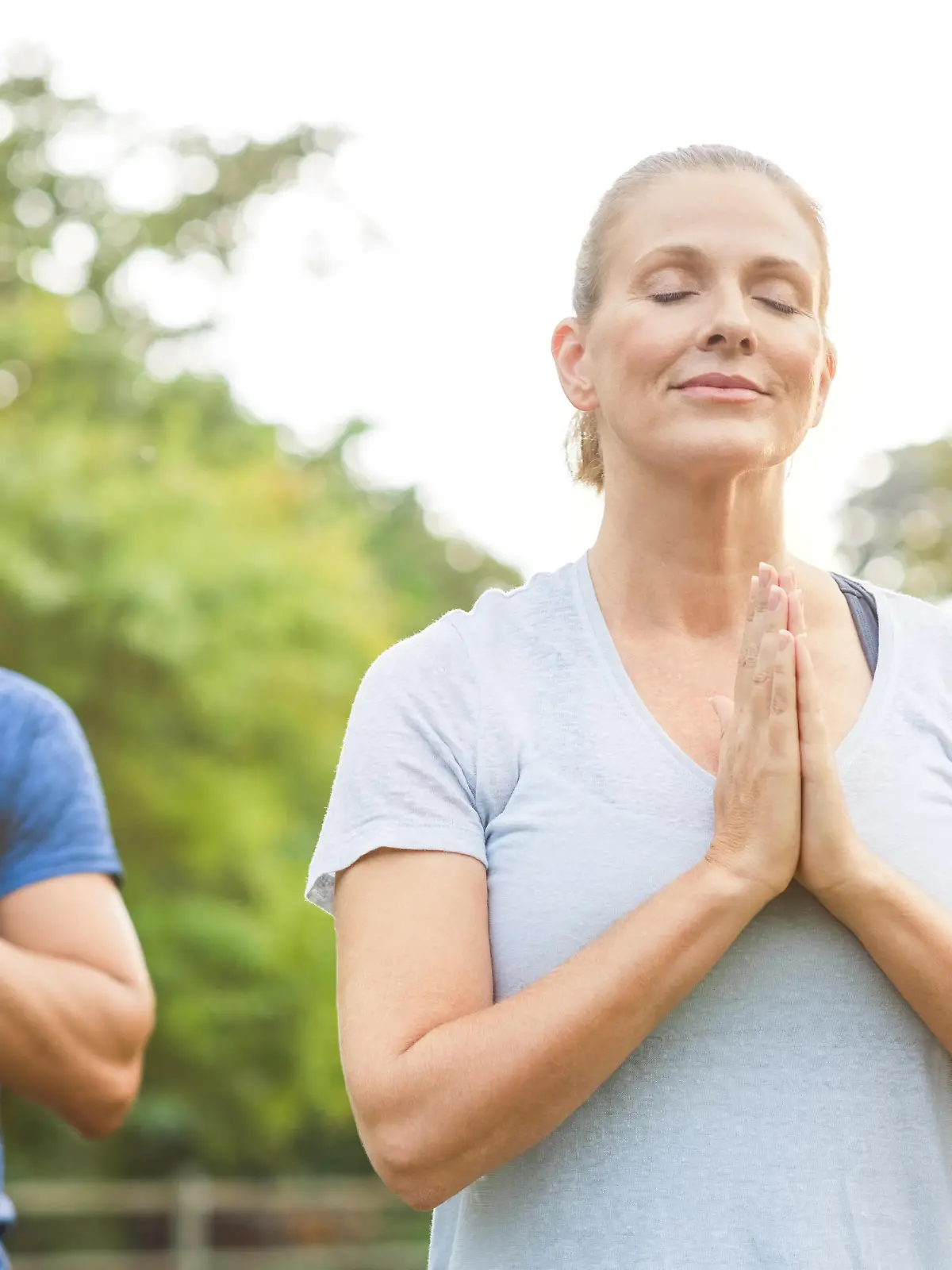 Three people at park meditating with joined hands and closed eyes. Senior woman and mature men doing breath exercise outdoor. Group of people doing yoga with joined hands and relaxing together."r