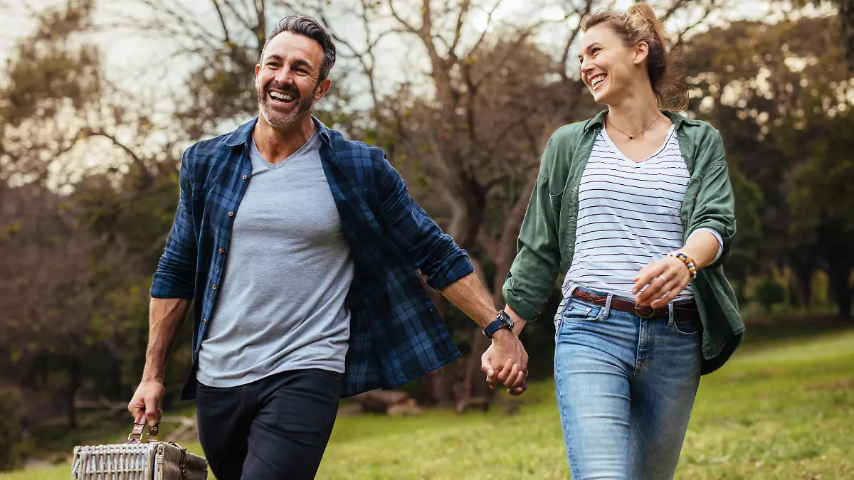 Happy couple walking in the park holding hand and carrying picnic basket. Loving couple going on a picnic at the park.