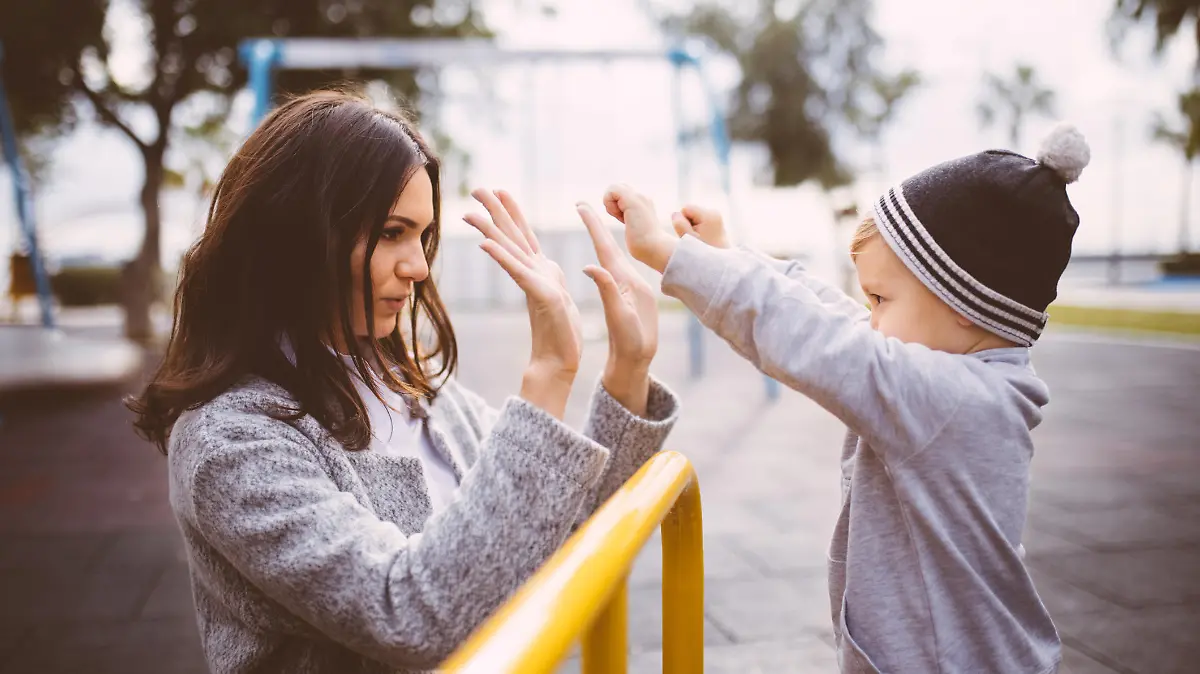 Young beautiful mom high fives young toddler at the park. Young mother cheers with young son.