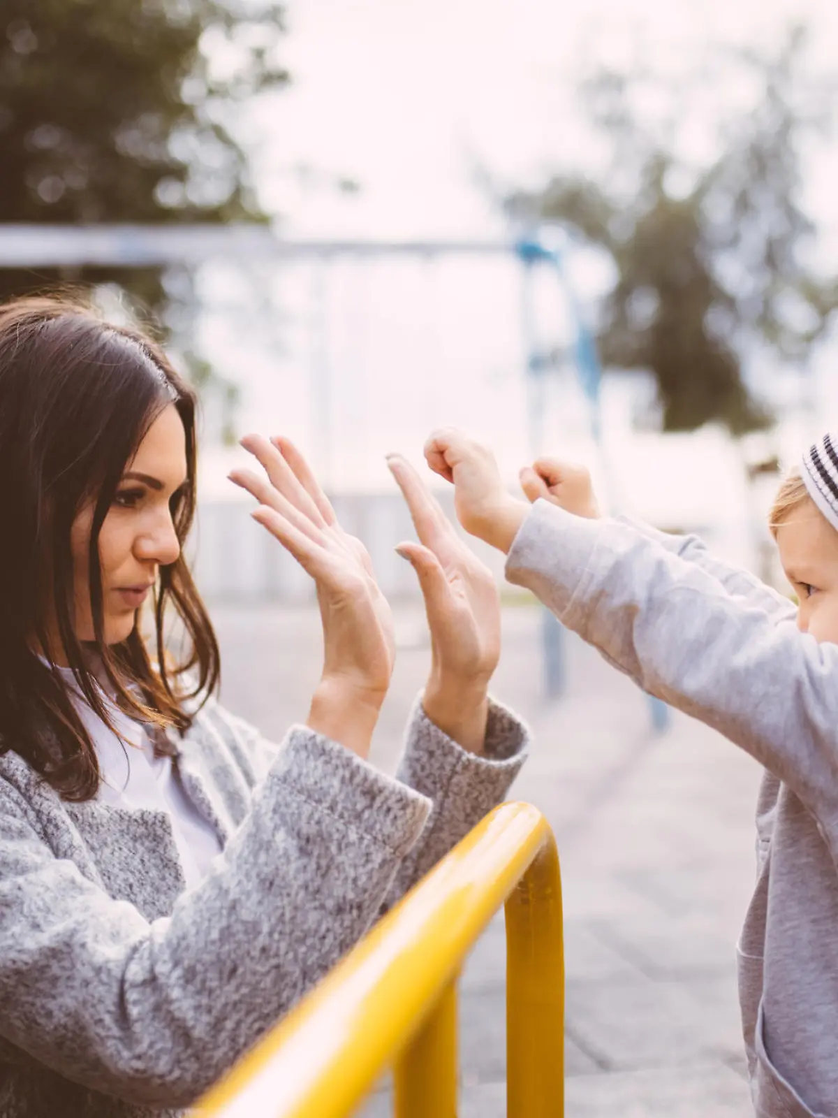 Young beautiful mom high fives young toddler at the park. Young mother cheers with young son.