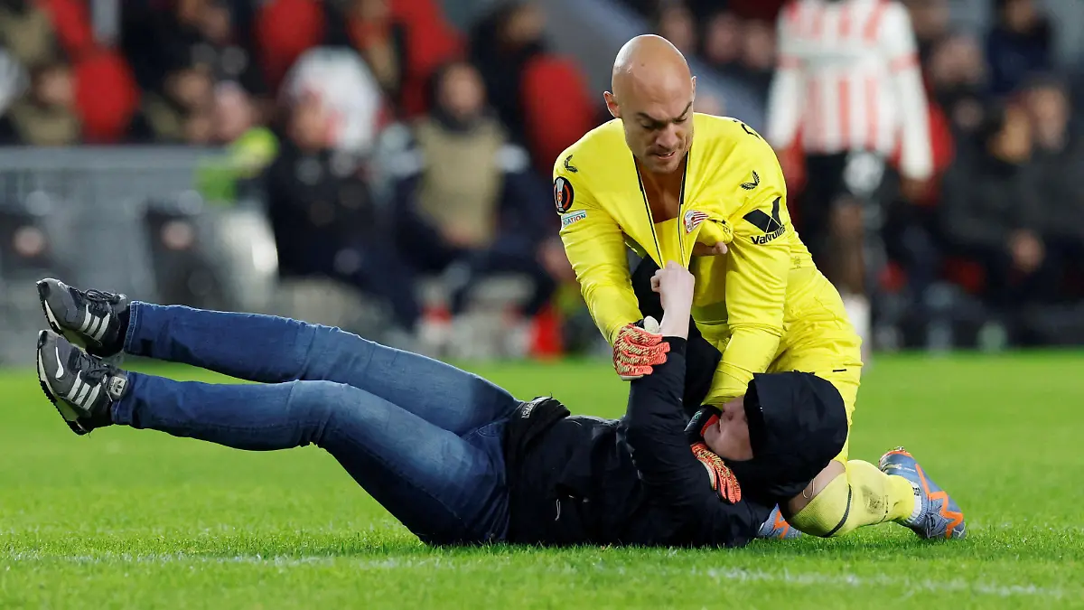 Soccer Football - Europa League - Play-Off Second Leg - PSV Eindhoven v Sevilla - Philips Stadion, Eindhoven, Netherlands - February 23, 2023 Pitch invader clashes with Sevilla's Marko Dmitrovic REUTERS/Piroschka Van De Wouw  REFILE - CORRECTING ID     TPX IMAGES OF THE DAY