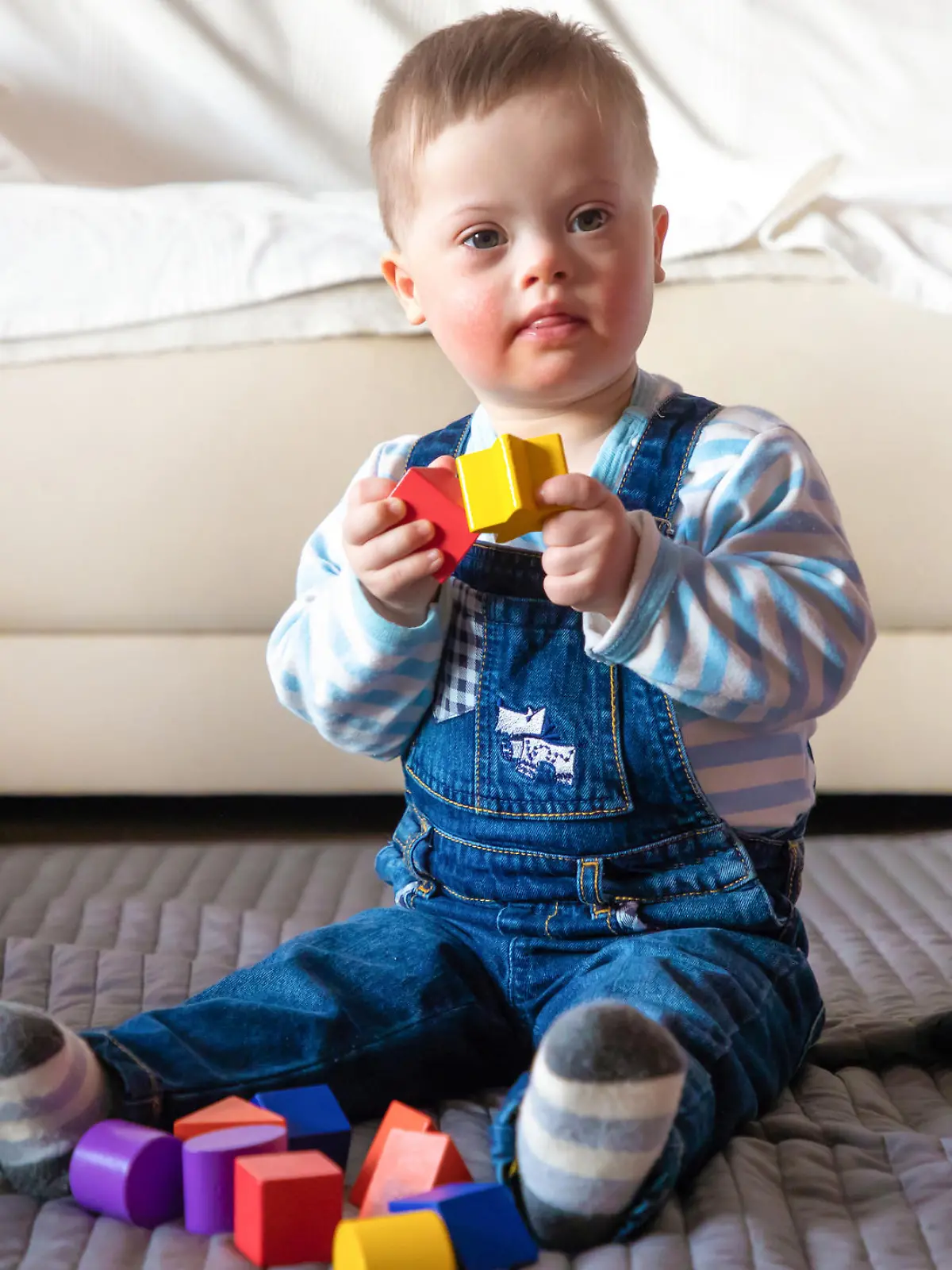 Portrait of cute baby boy with Down syndrome playing in home living room