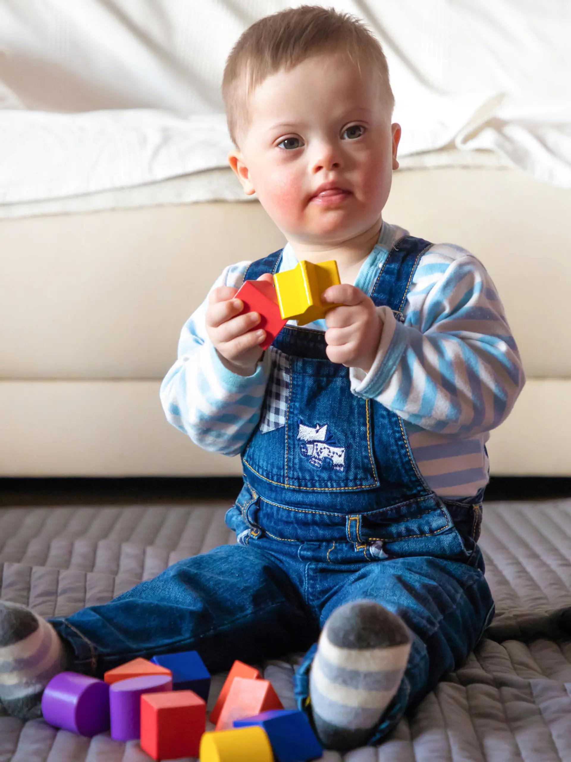 Portrait of cute baby boy with Down syndrome playing in home living room