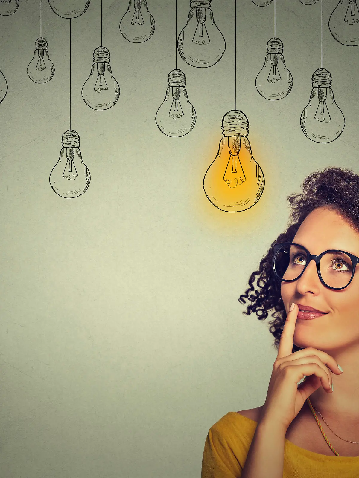 Portrait thinking woman in glasses looking up with light idea bulb above head isolated on gray wall background