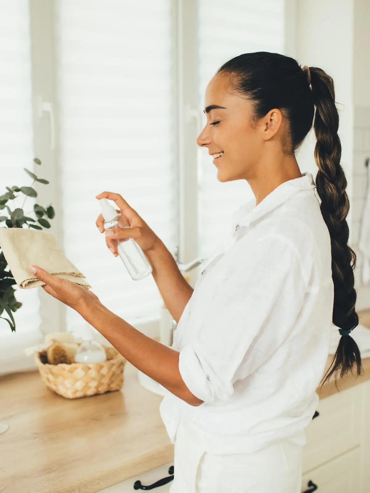 Young woman cleaning house using spray and natural rag standing in a kitchen of a cozy house.