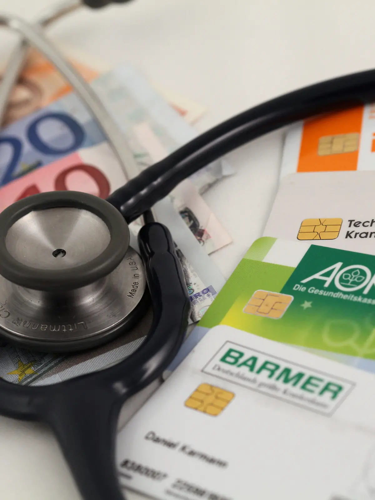 ARCHIV - ILLUSTRATION - Die Versichertenkarten der deutschen Krankenkassen DAK, AOK, Barmer und Techniker Krankenkasse TK liegen mit einem 50, 20, zehn und fünf Euro-Schein unter einem Stethoskop, aufgenommen am 17.12.2009. Die gesetzlichen Krankenkassen haben nach einem Pressebericht im ersten Halbjahr einen Überschuss von mehr als 1,2 Milliarden Euro erzielt. Foto: Daniel Karmann/dpa (zu dpa 0016 vom 30.08.2013) +++(c) dpa - Bildfunk+++