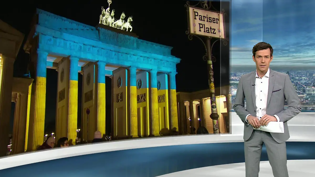 RTL-Moderator Maik Meuser steht im Studio, hinter ihm sieht man das Brandenburger Tor, das in gelb und blau angestrahlt wird.