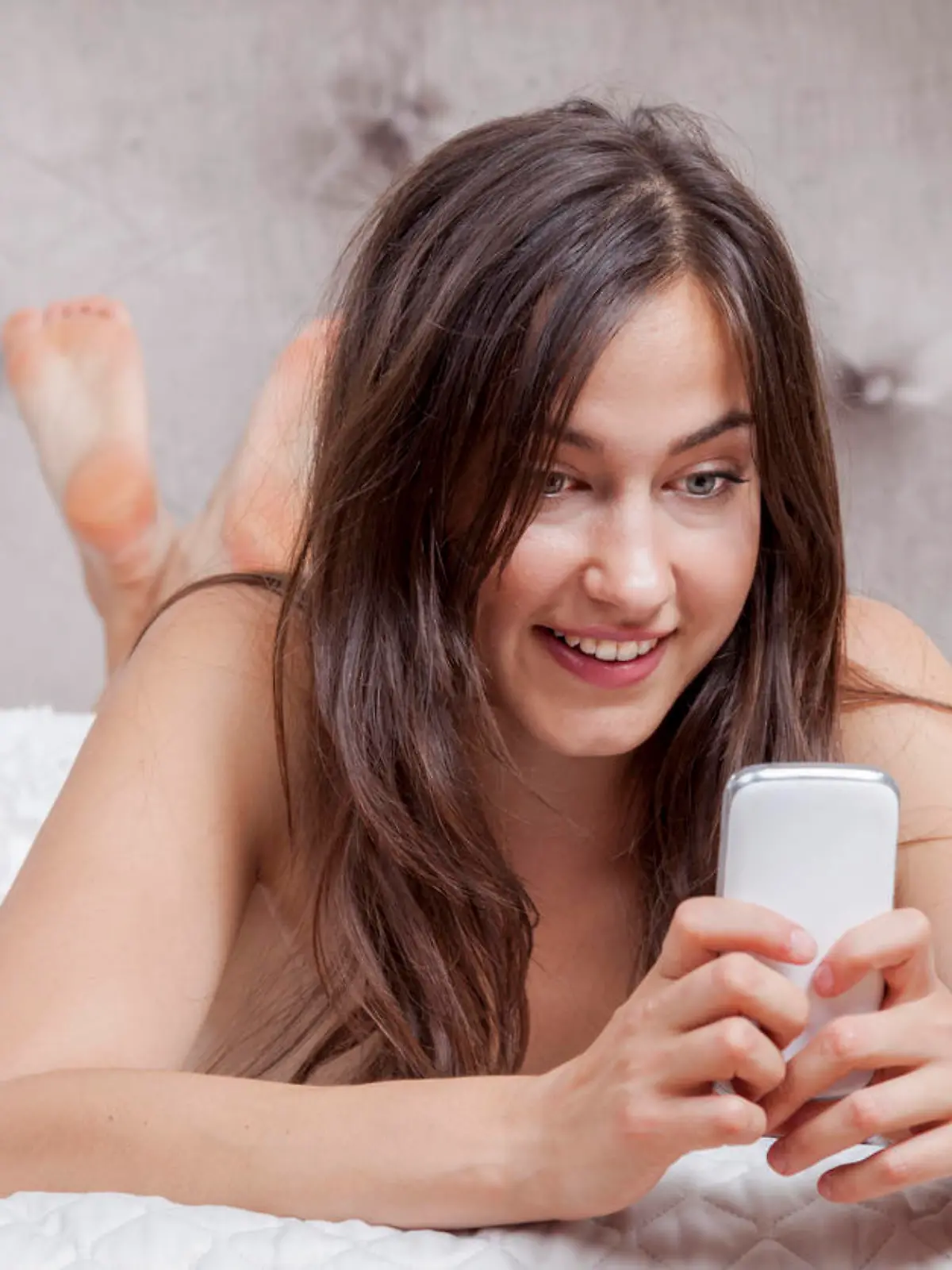 Junge Frau mit Smartphone auf Bett