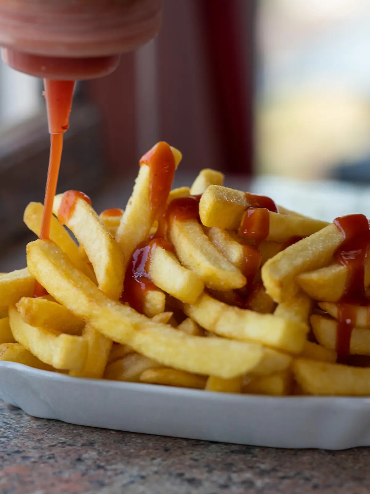 Ketchup wird auf Pommes verteilt.