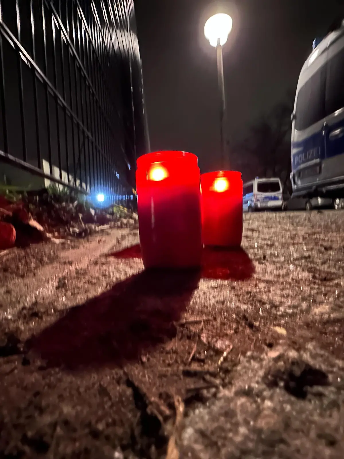 21.02.2023, Berlin: Brennende Kerzen stehen an einem Park in Pankow neben Polizeifahrzeugen. Das vermisste vierjährige Mädchen aus Berlin ist tot. Es sei am Abend mit Verletzungen von Passanten im Bürgerpark Pankow gefunden worden, sagte ein Polizeisprecher. Rettungskräfte hätten versucht, das Kind zu reanimieren. Es sei dann im Krankenhaus verstorben. Ein 19 Jahre alter Tatverdächtiger sei bereits festgenommen worden. (Zu dpa «Vermisste Vierjährige in Berlin tot - Polizei vermutet Tötungsdelikt») Foto: Paul Zinken/dpa +++ dpa-Bildfunk +++