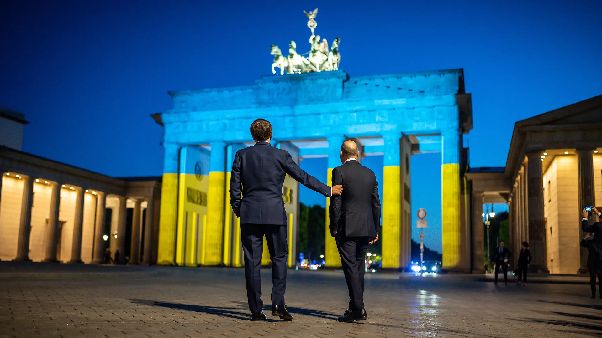 Bundeskanzler Olaf Scholz (r, SPD) und Frankreichs Präsident Emmanuel Macron stehen nach einem Treffen vor dem Brandenburger Tor. Aus Anlass des Europatages ist das Brandenburger Tor in den ukrainischen Nationalfarben beleuchtet.