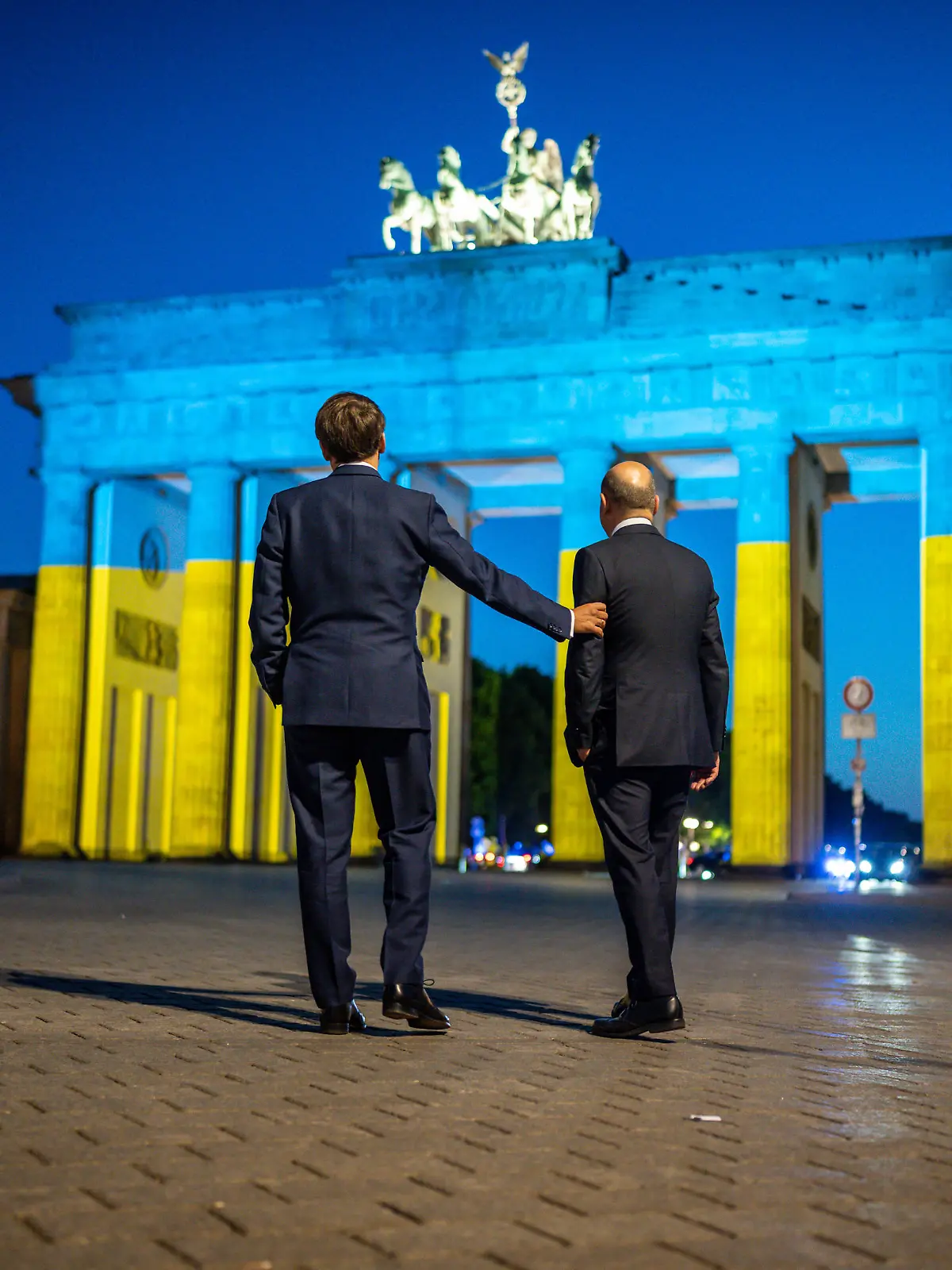 Bundeskanzler Olaf Scholz (r, SPD) und Frankreichs Präsident Emmanuel Macron stehen nach einem Treffen vor dem Brandenburger Tor. Aus Anlass des Europatages ist das Brandenburger Tor in den ukrainischen Nationalfarben beleuchtet.