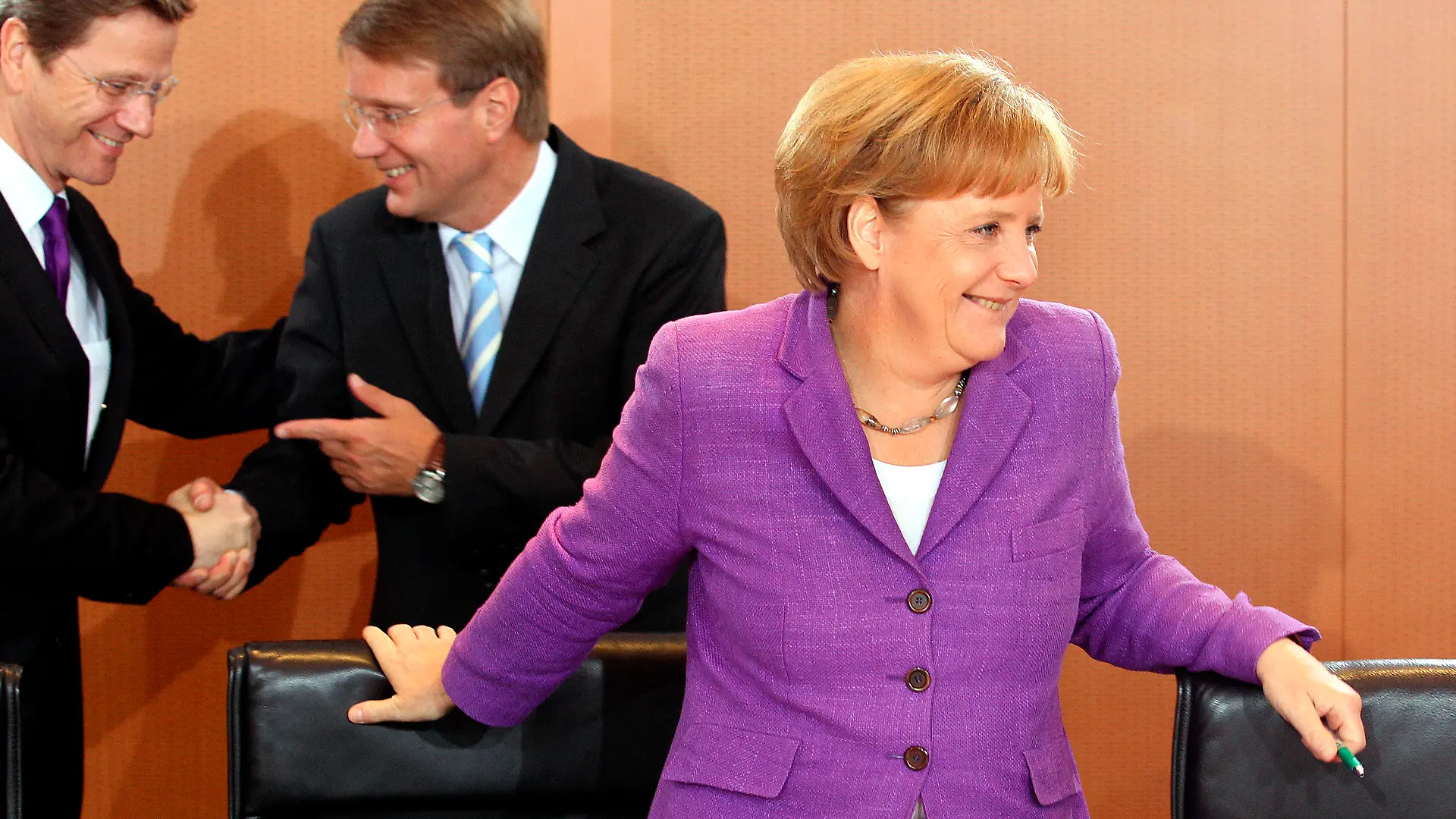 Lachend steht Bundeskanzlerin Angela Merkel (CDU) am Mittwoch (02.06.2010) zu Beginn der Kabinettssitzung im Bundeskanzleramt in Berlin am Konferenztisch, während sich im Hintergrund Bundesaußenminister Guido Westerwelle (FDP, l) und Kanzleramtsminister Ronald Pofalla (CDU) begrüßen. Foto: Wolfgang Kumm dpa/lbn  +++(c) dpa - Bildfunk+++
